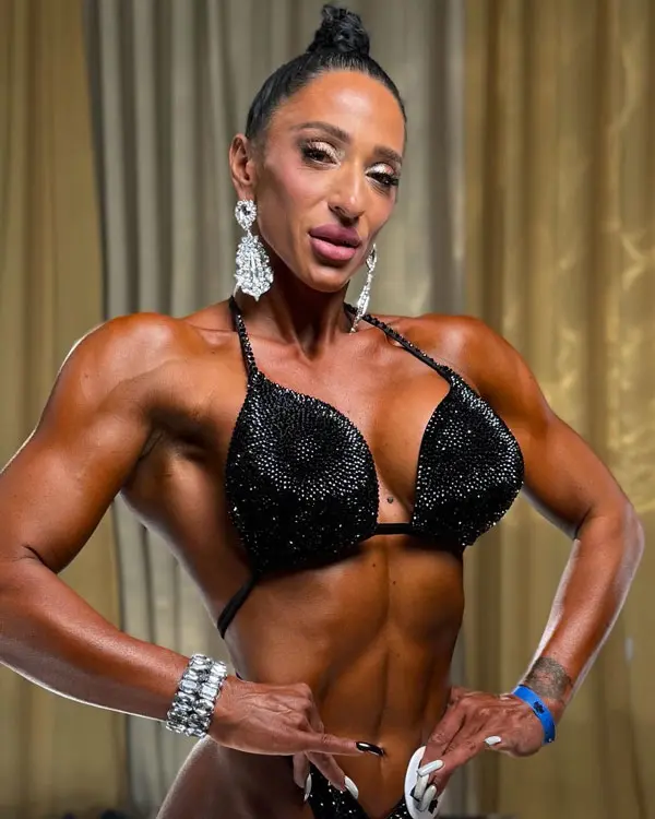 Marina Nikolaeva bodybuilding competition backstage posing in stage bikini, muscular and defined physique with feminine presentation